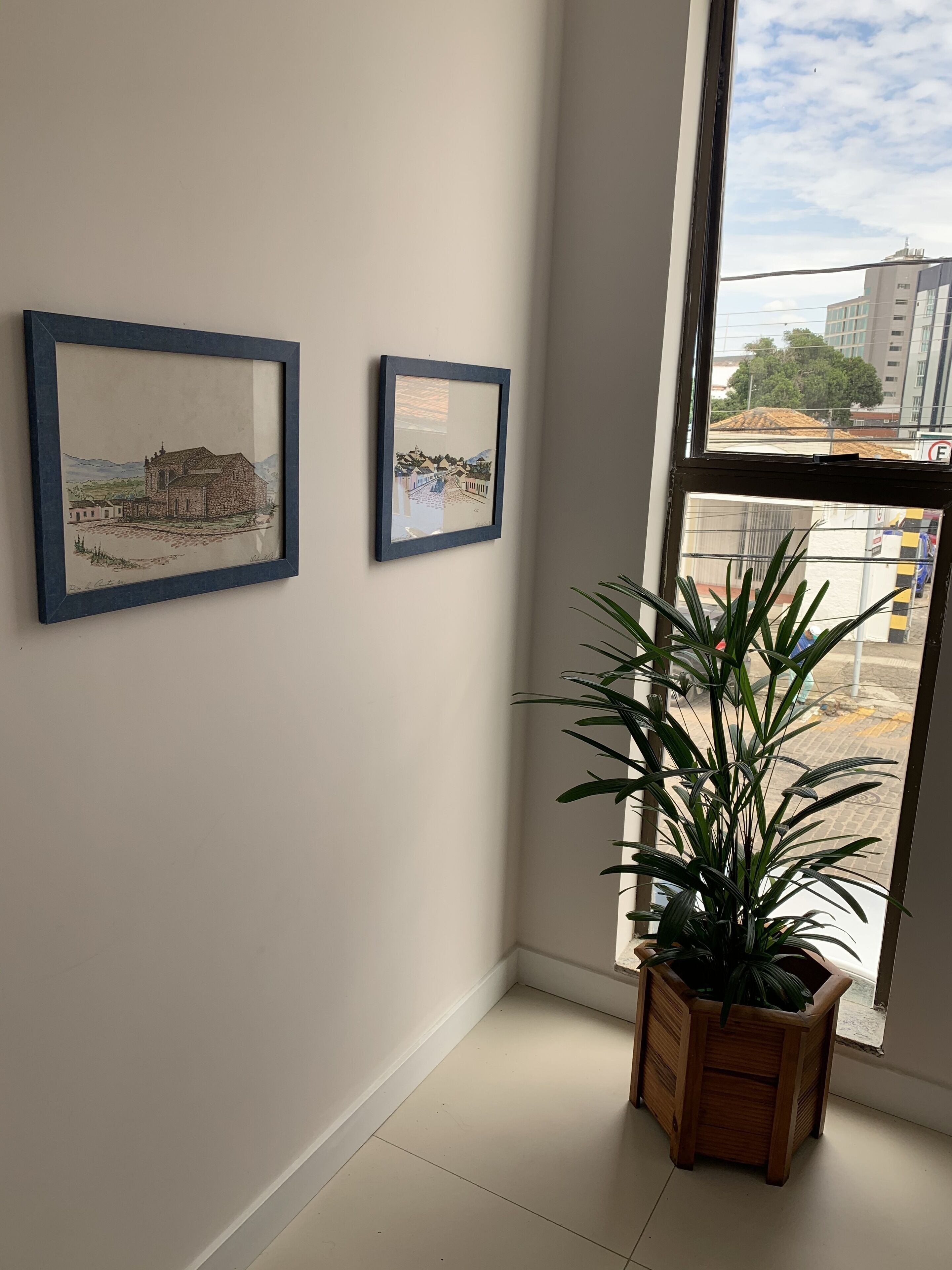 A room with two framed artworks on the wall, a potted plant by the window, and a view of a construction site outside.