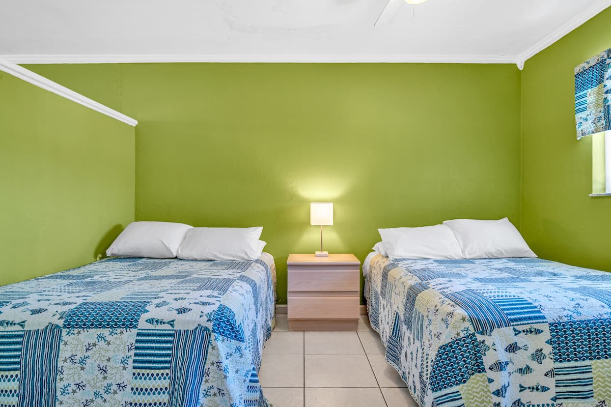 Een kamer met twee bedden, groene wanden, een nachtkastje met een lamp en een bed met een decoratief sprei.