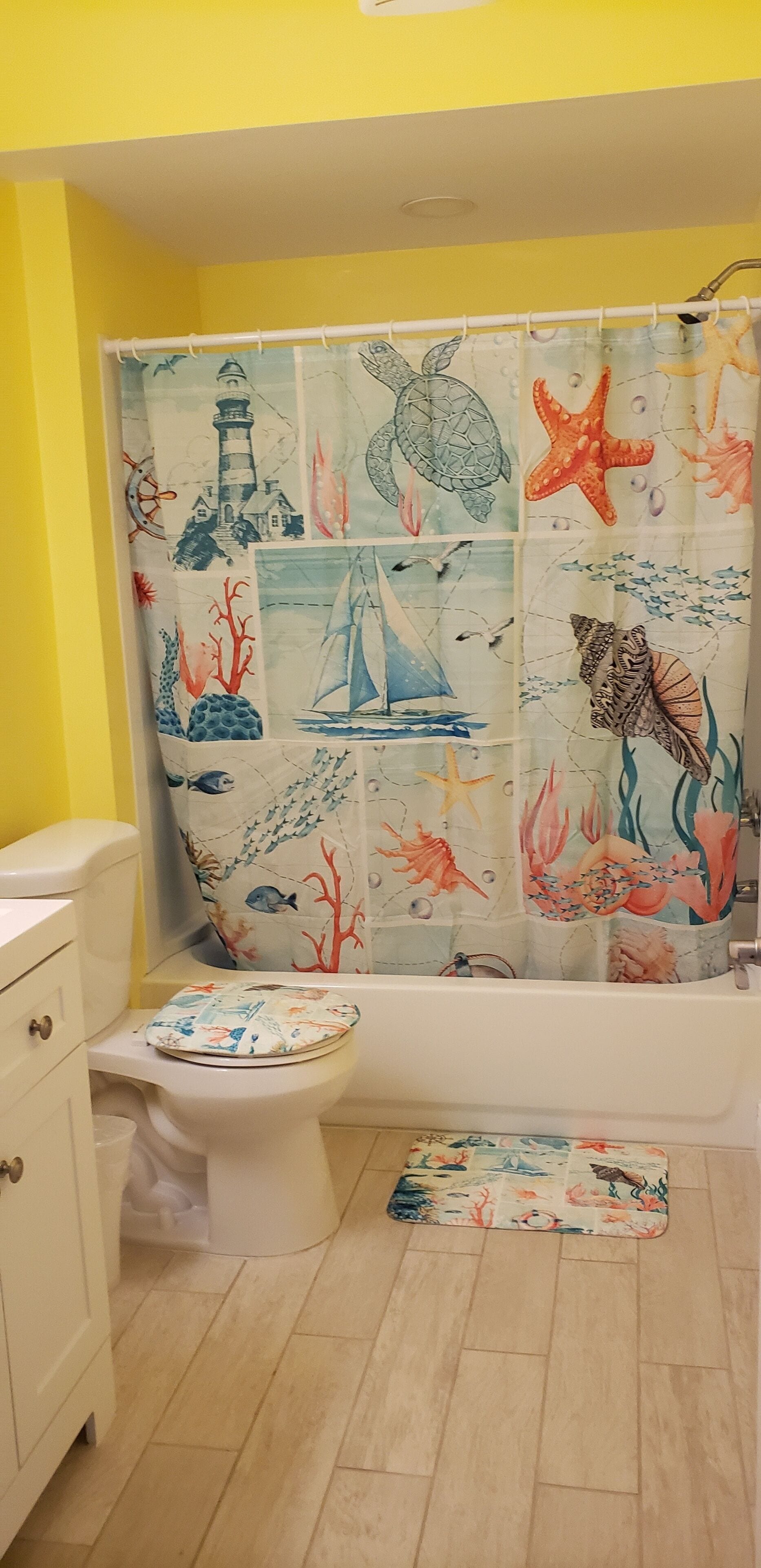 Ein Badezimmer mit einer maritim gestalteten Duschvorhangs, einer Toilette mit dekorativem Sitz und einem Holzboden.