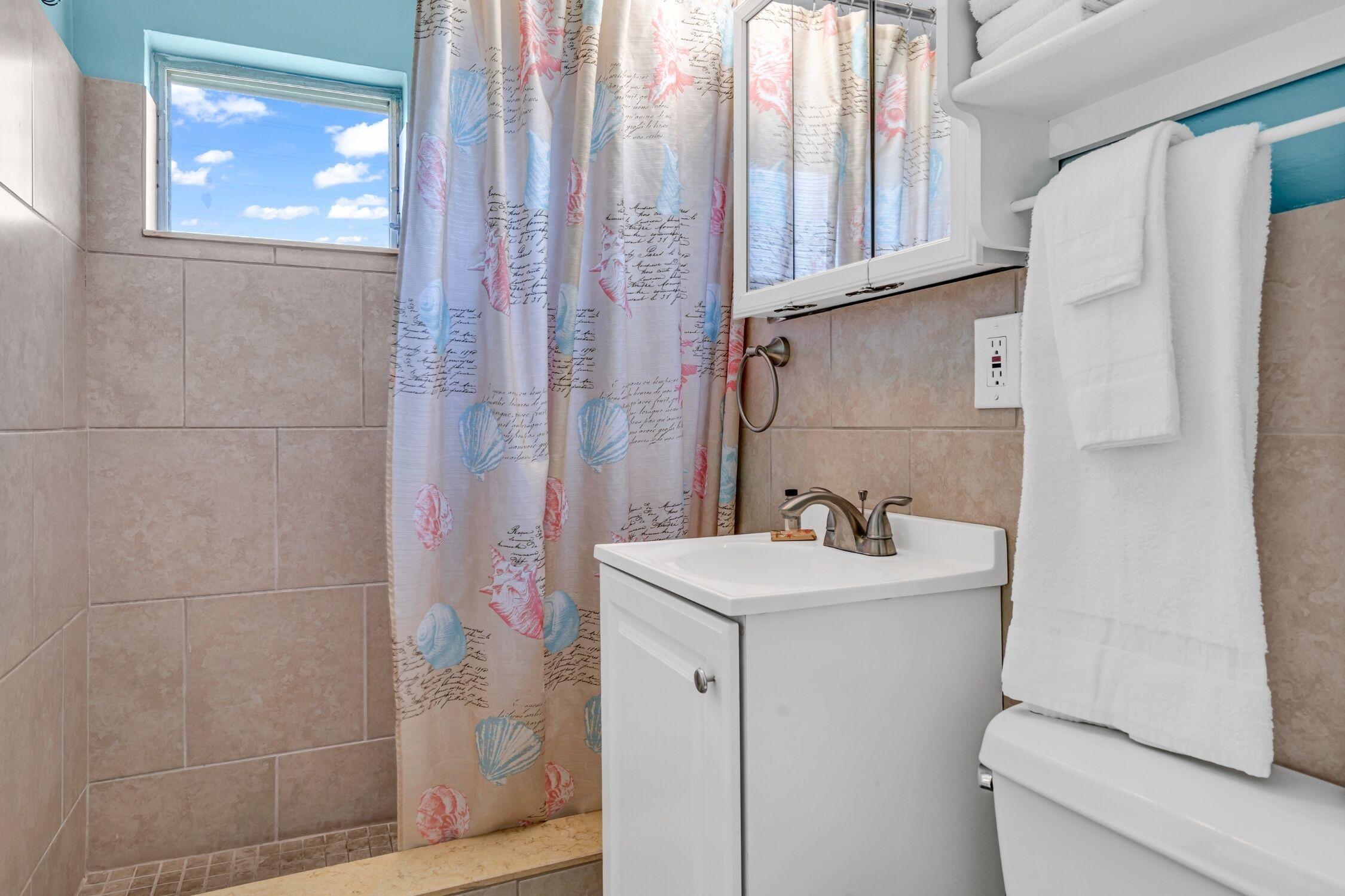 Ein Badezimmer mit Fenster, Waschbecken, Toilette und einer Duschvorhang mit floralem Muster.