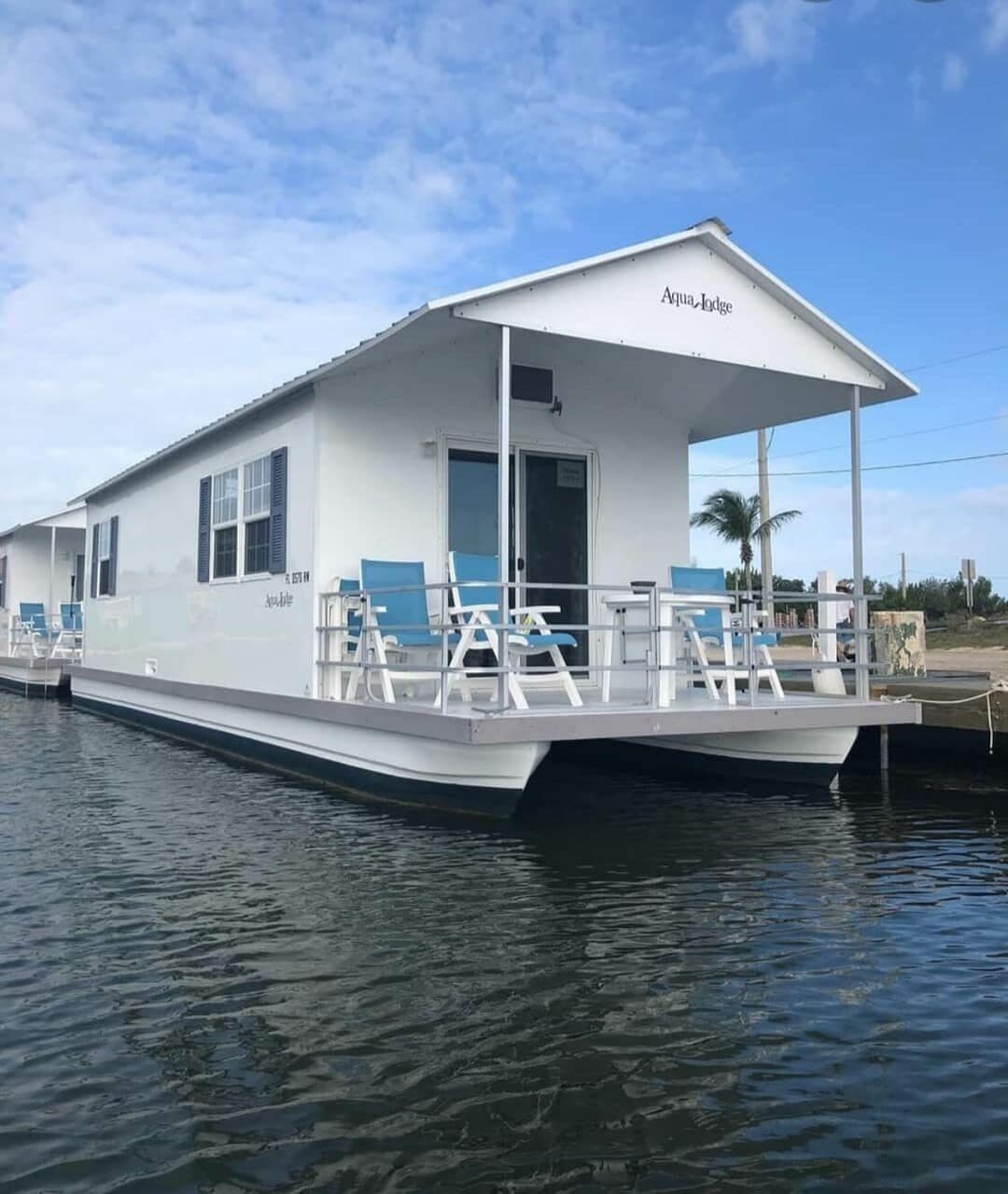 Une péniche à usage résidentiel, dotée d’une terrasse couverte, baptisée « Aqua Lodge », et comprenant un espace de détente avec des fauteuils et des tables.
