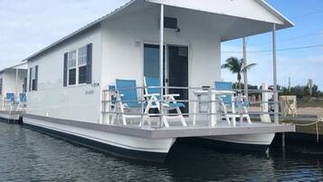 Une péniche à usage résidentiel, dotée d’une terrasse couverte, baptisée « Aqua Lodge », et comprenant un espace de détente avec des fauteuils et des tables.