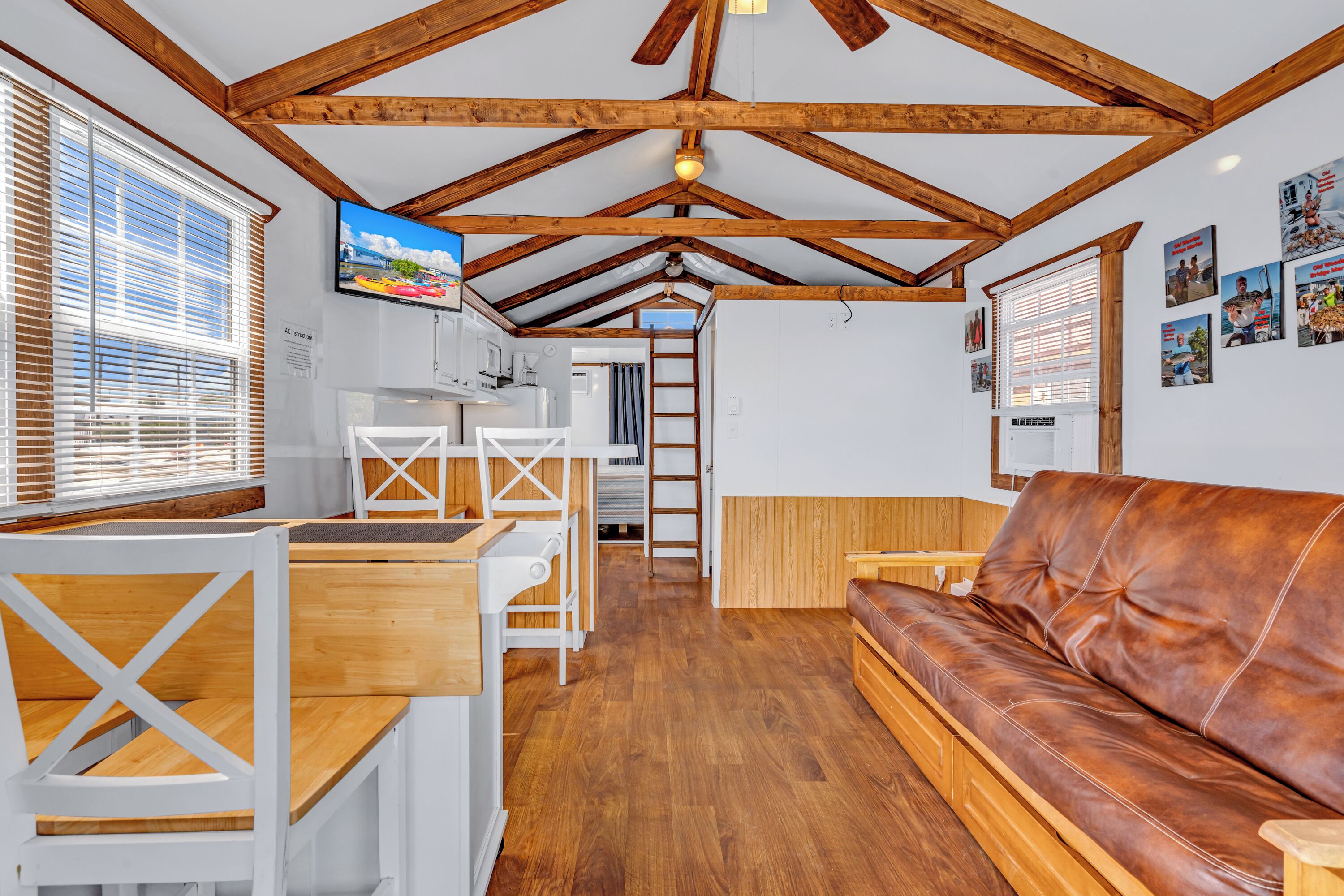 A cozy interior with a wooden ceiling, a brown leather sofa, a wooden dining table, and white chairs.