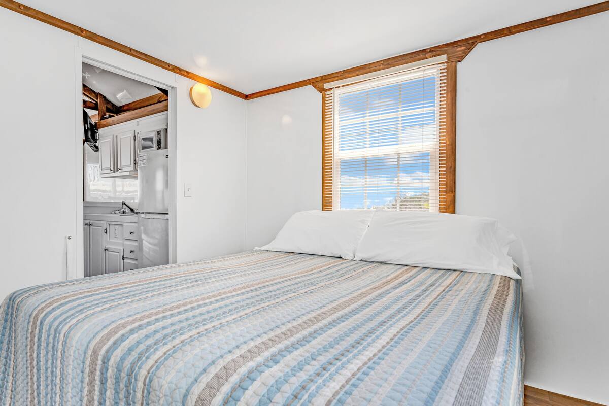 Een slaapkamer met een bed, een raam met jaloezieën en uitzicht op buiten.