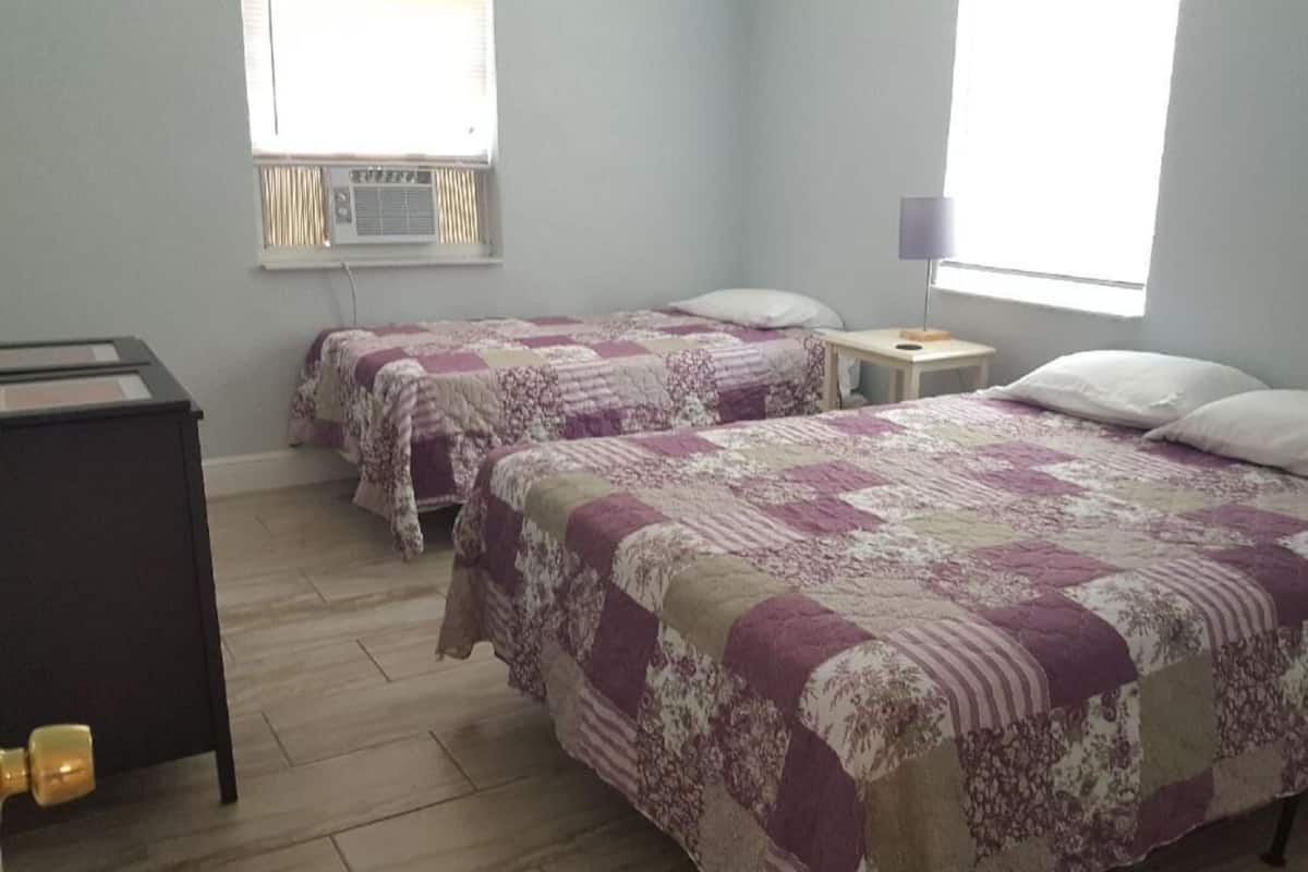 Een kamer met twee bedden, een klein tafeltje en een airconditioning aan de muur.