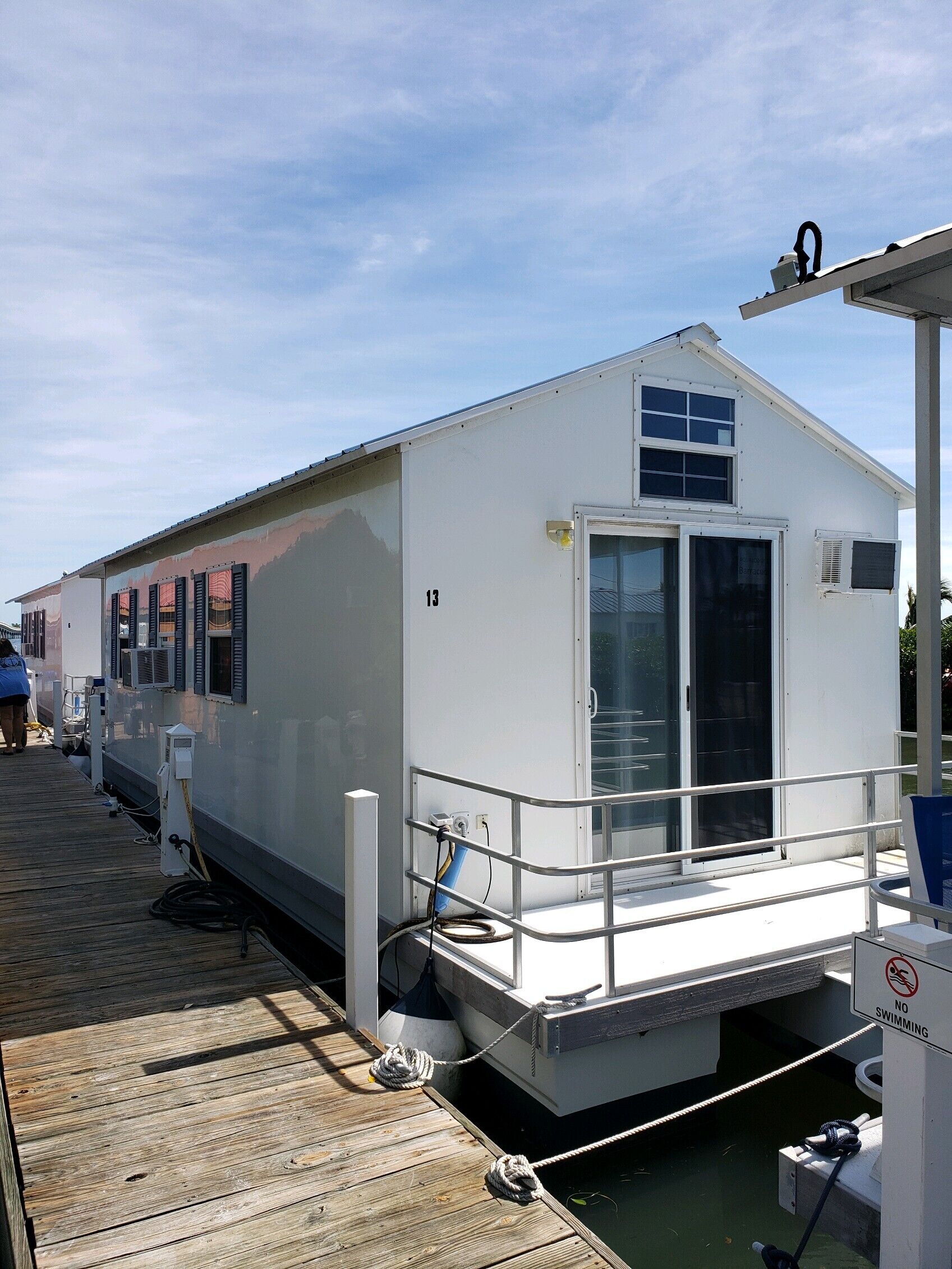 A white docked boat with a cabin, numbered 13, and a no swimming sign.