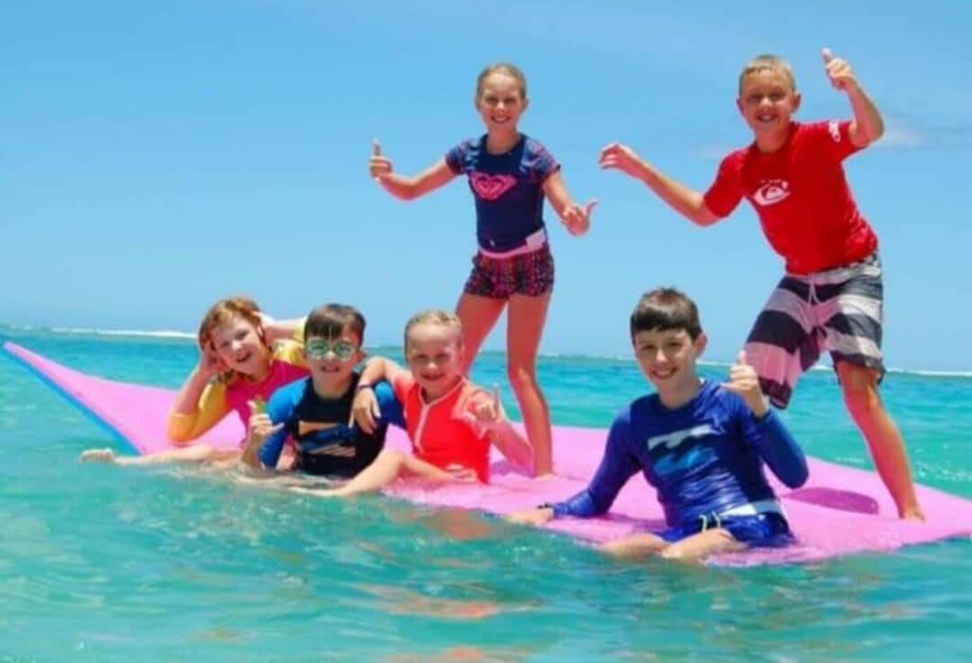 A group of people on a pink surfboard in the ocean.