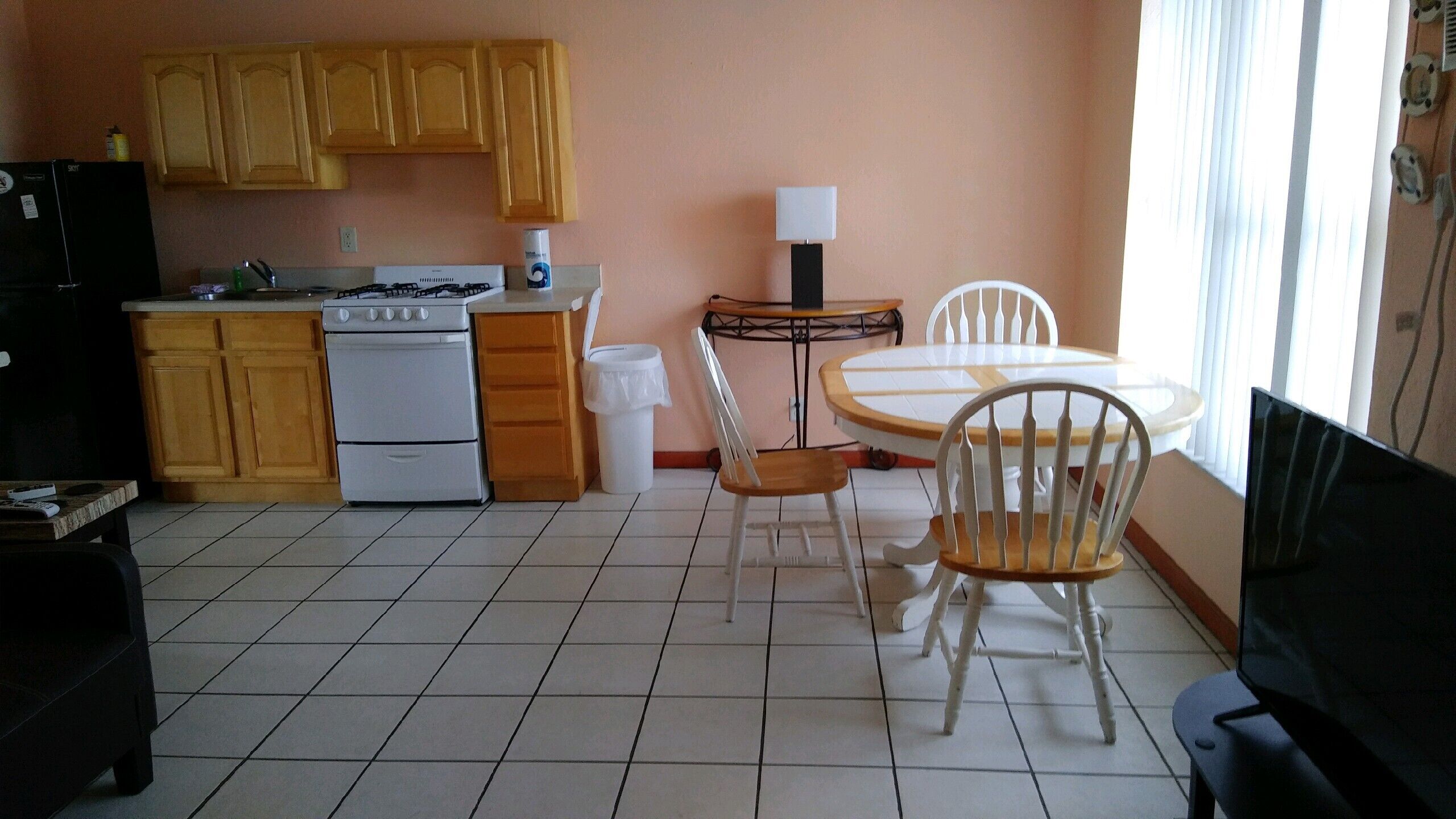 A compact kitchen with wooden cabinets, a gas stove, a white refrigerator, and a dining area with a table and chairs.