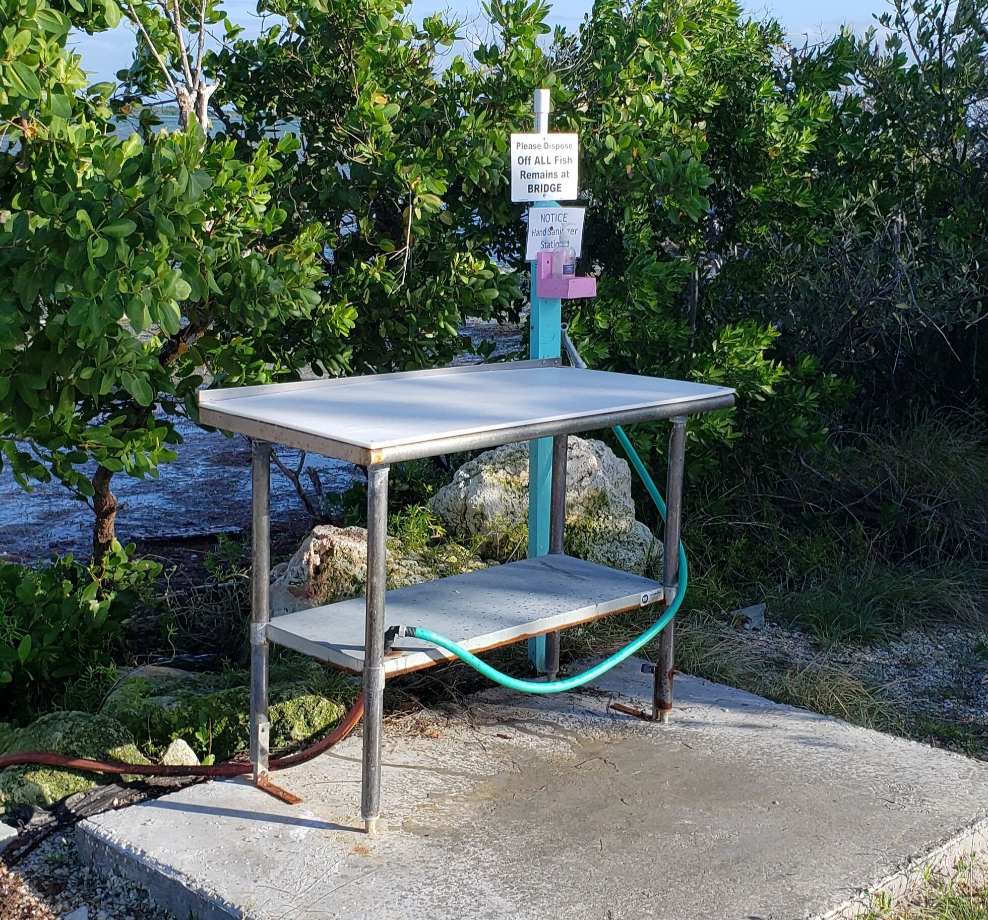 A metal table with a sign above it, a hand sanitizer station, and a hose connected to the table.