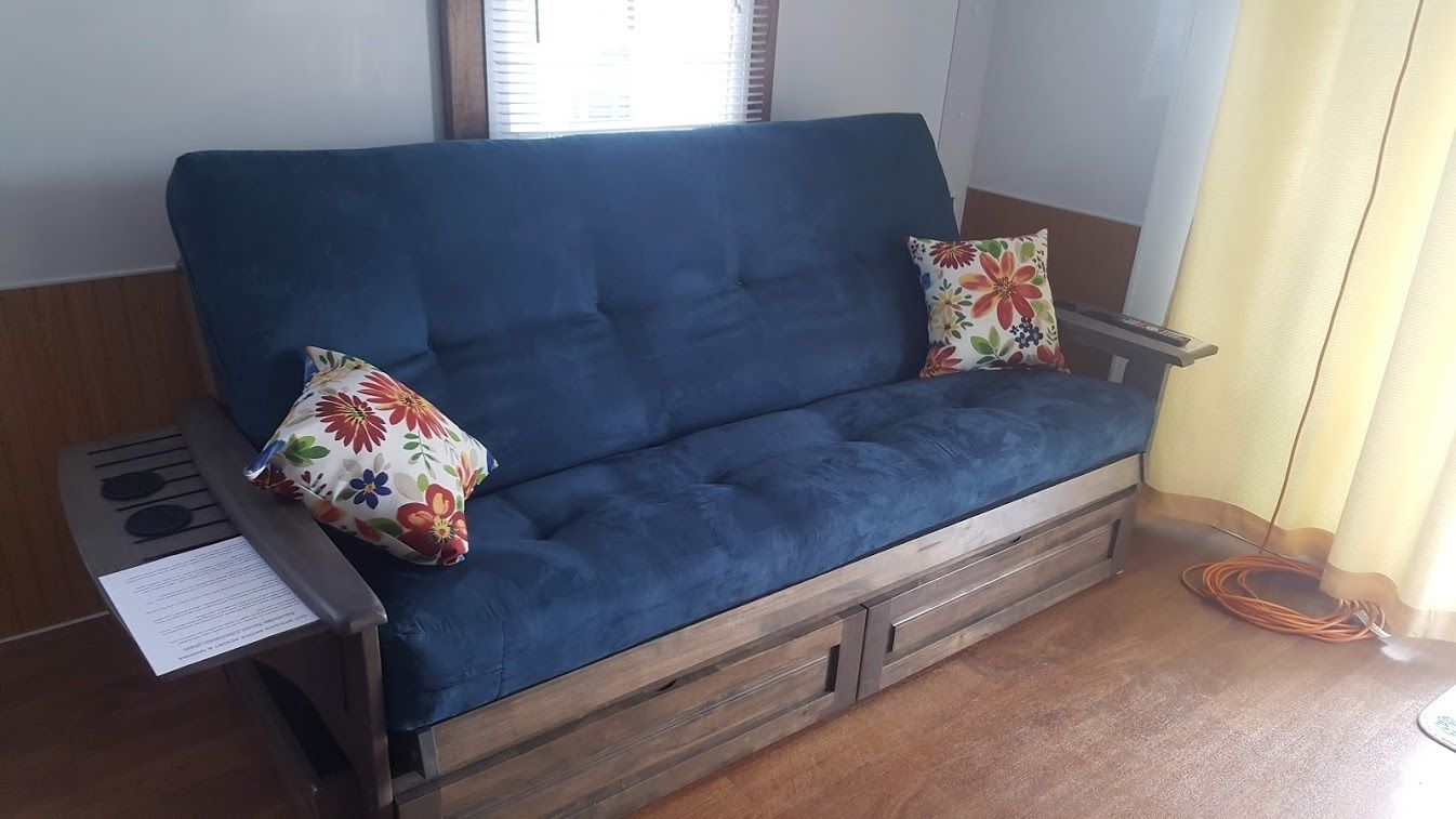A blue sofa with floral cushions, a wooden side table with a remote control, and a power cord on the floor.