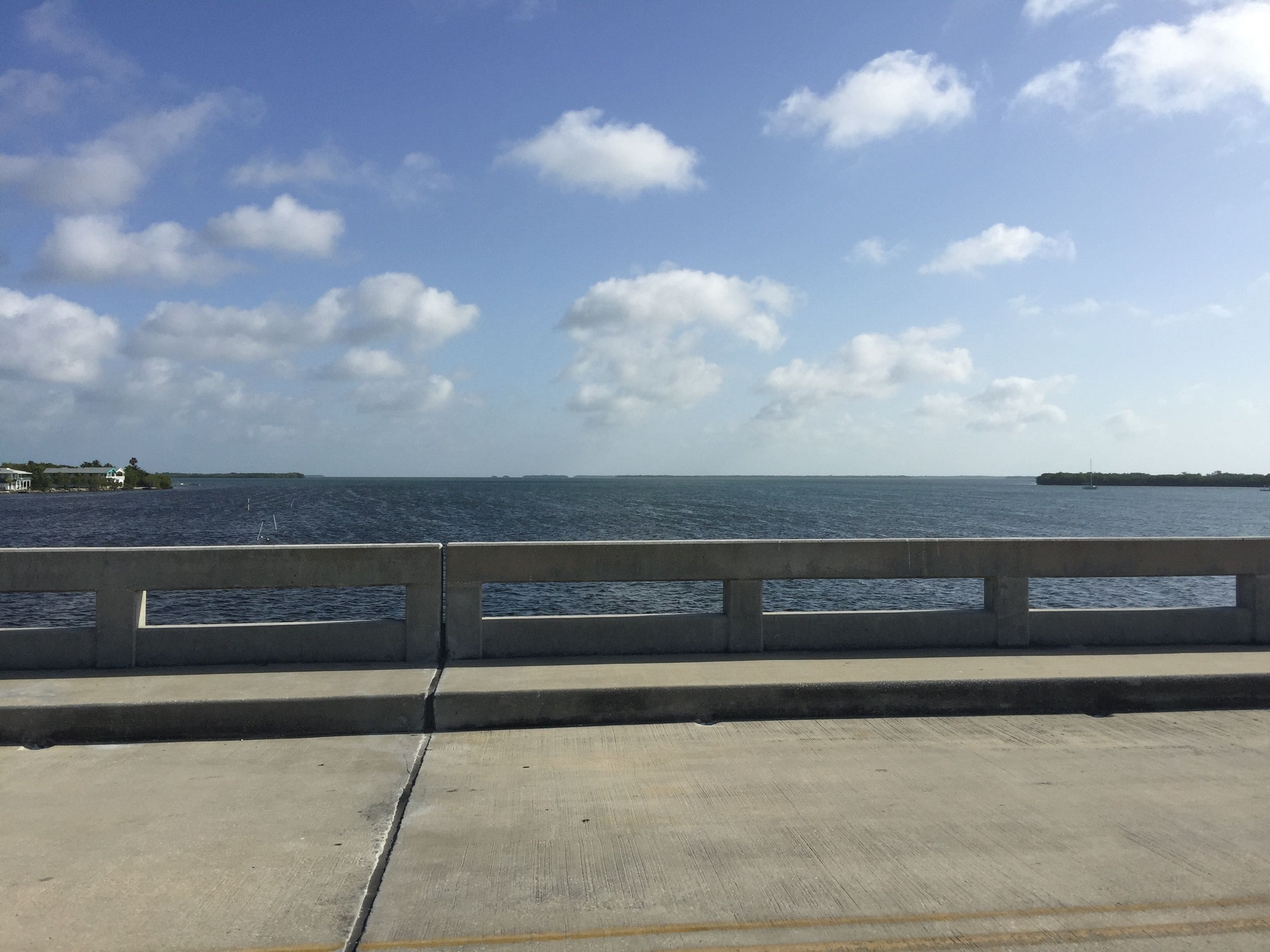 A concrete bridge with a railing, overlooking a calm body of water with a distant shoreline.