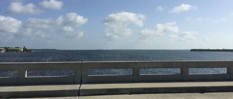 A concrete bridge with a railing, overlooking a calm body of water with a distant shoreline.