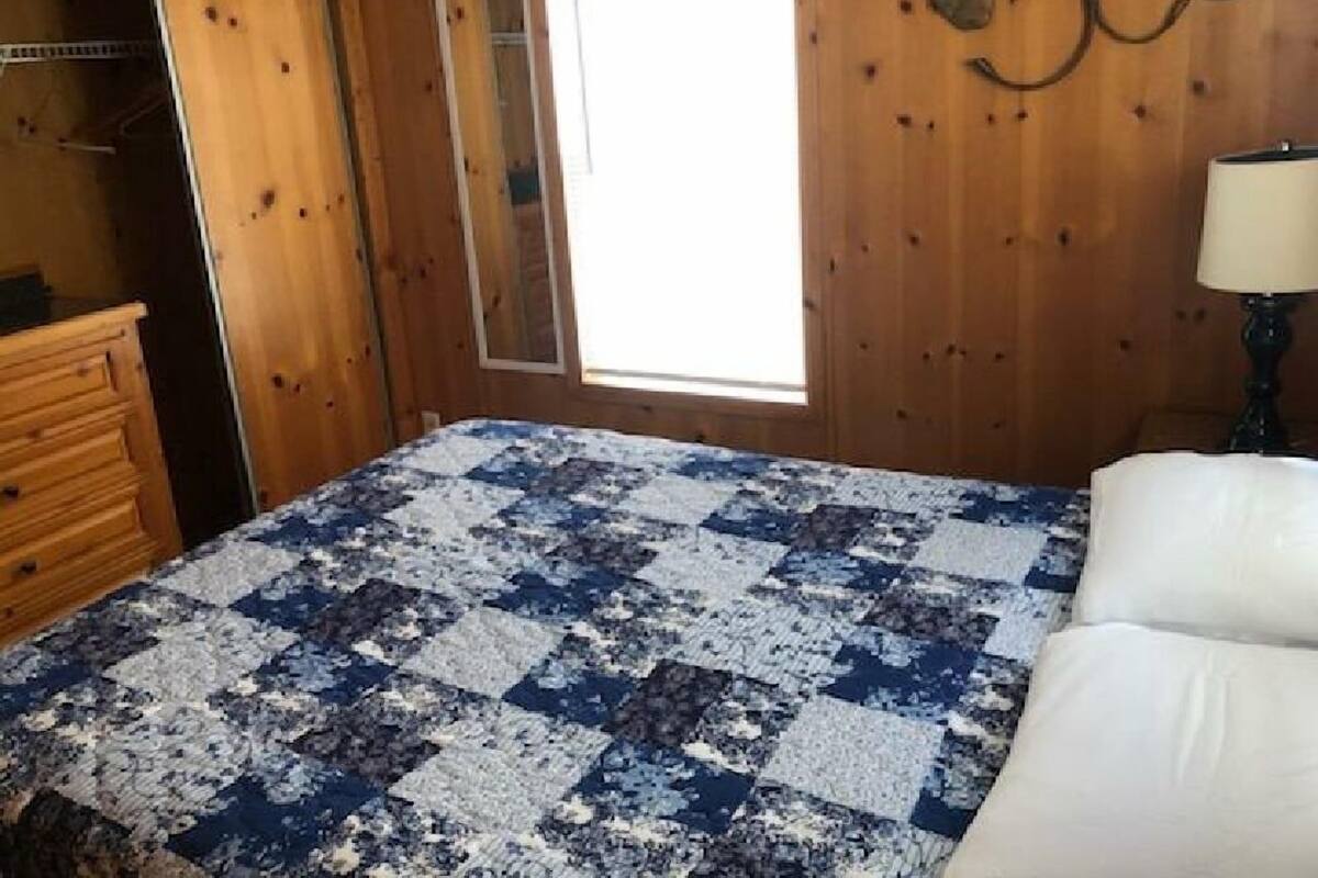 Een slaapkamer met een houten wand, een raam, een bed met wit beddengoed en een dressoir.