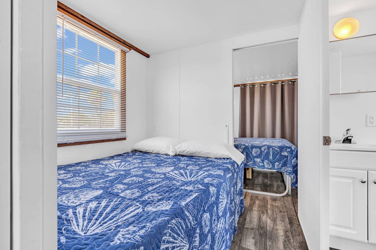Een compacte kamer met twee bedden, een kleine kitchenette en een raam met zonwering.