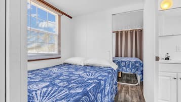 Ein kleines Zimmer mit zwei Betten, einer kleinen Küchenzeile und einem Fenster mit Jalousien.
