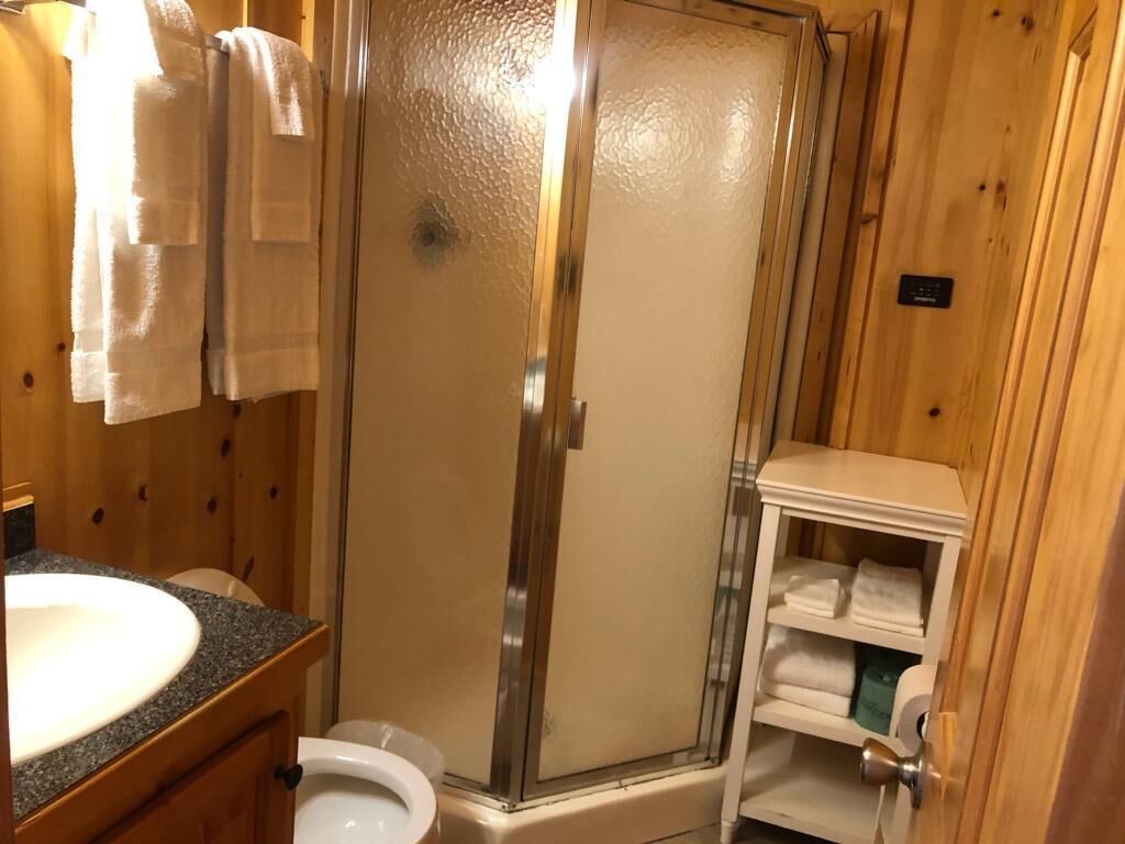 A wooden bathroom with a glass shower enclosure, a sink, and a toilet.