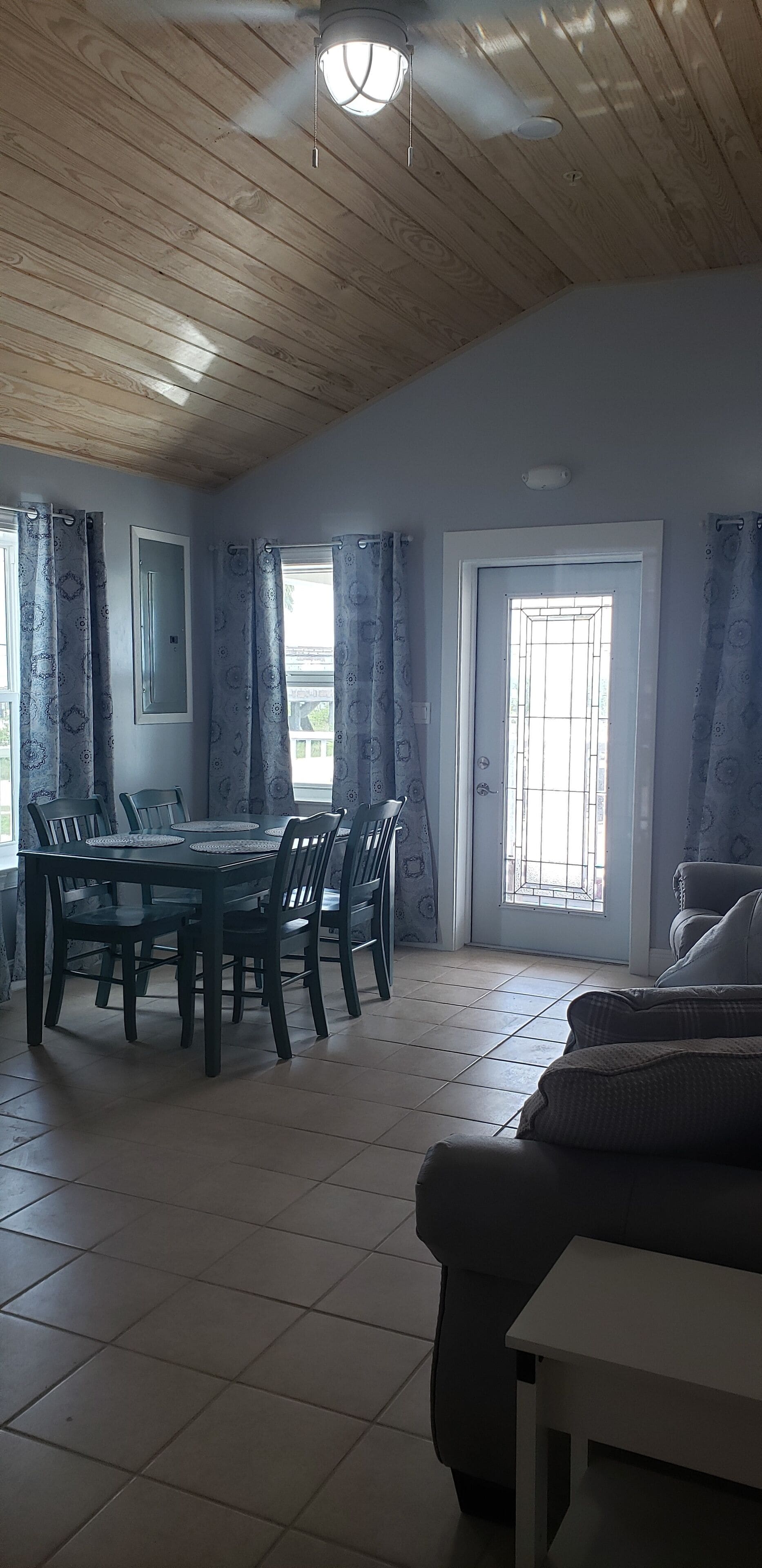 Un comedor con techo de madera, una mesa de comedor con sillas y vistas a través de una ventana con cortinas.
