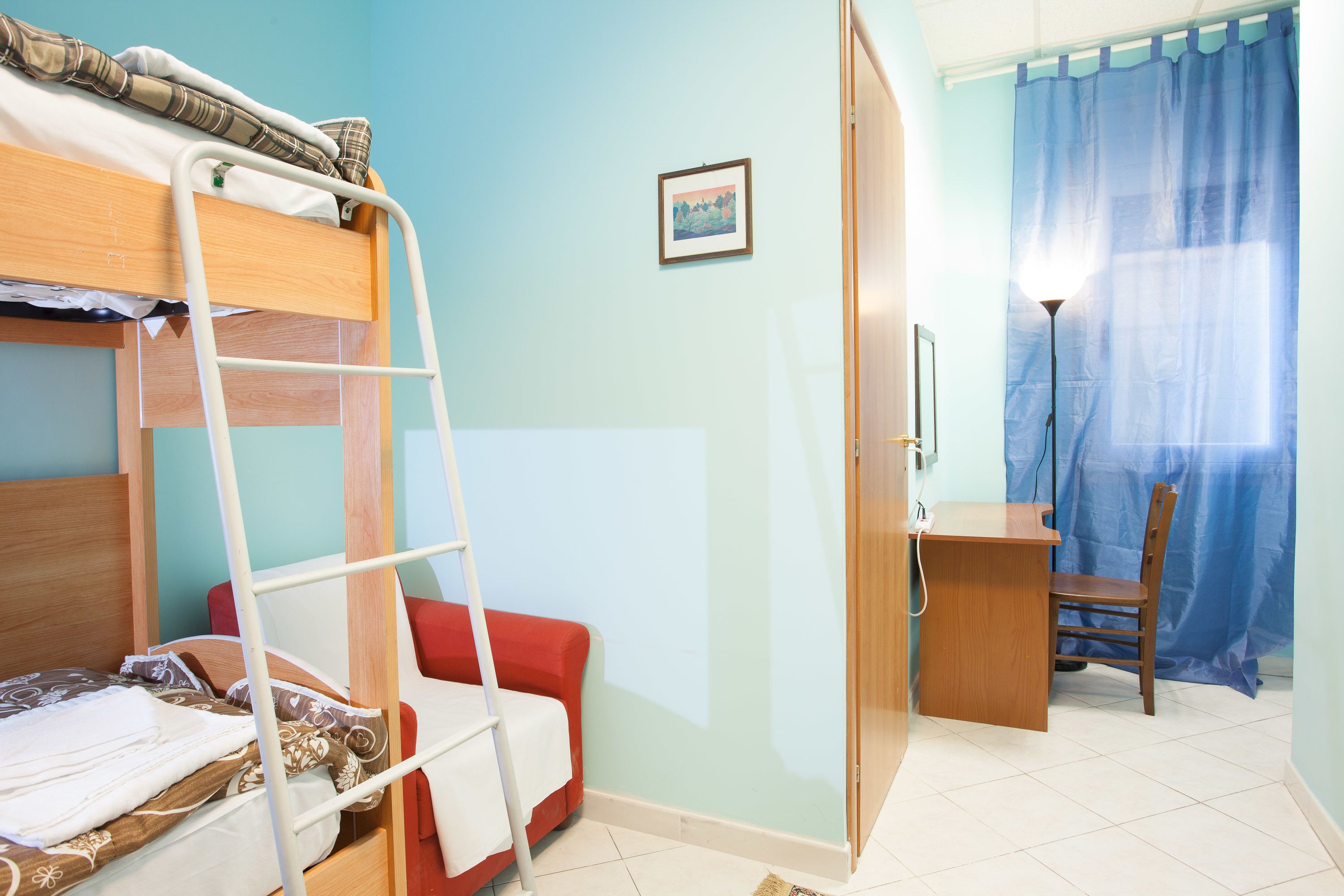 Un lit superposé avec une échelle, un bureau avec une chaise, une lampe et une fenêtre avec des rideaux.