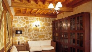 A cozy room with a stone wall, wooden ceiling beams, a sofa, a wooden cabinet, and a table. - La Casona de Doña Petra (Villarmentero de Campos)