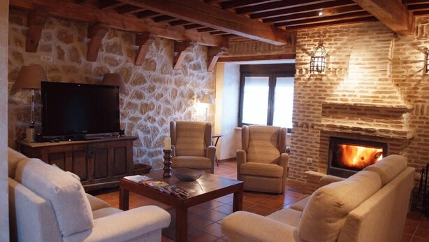 A cozy living room with stone walls, a fireplace, and comfortable seating. - La Casona de Doña Petra (Villarmentero de Campos)