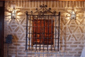 Un muro de piedra con una reja de metal y dos faroles fijados a la pared.
