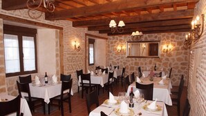 A restaurant with stone walls, wooden beams, and white tablecloths. Tables are set with wine glasses, plates, and cutlery. - La Casona de Doña Petra (Villarmentero de Campos)