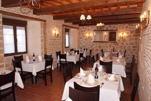 Un restaurante con paredes de piedra, vigas de madera y manteles blancos. Las mesas están preparadas con copas de vino, platos y cubiertos.