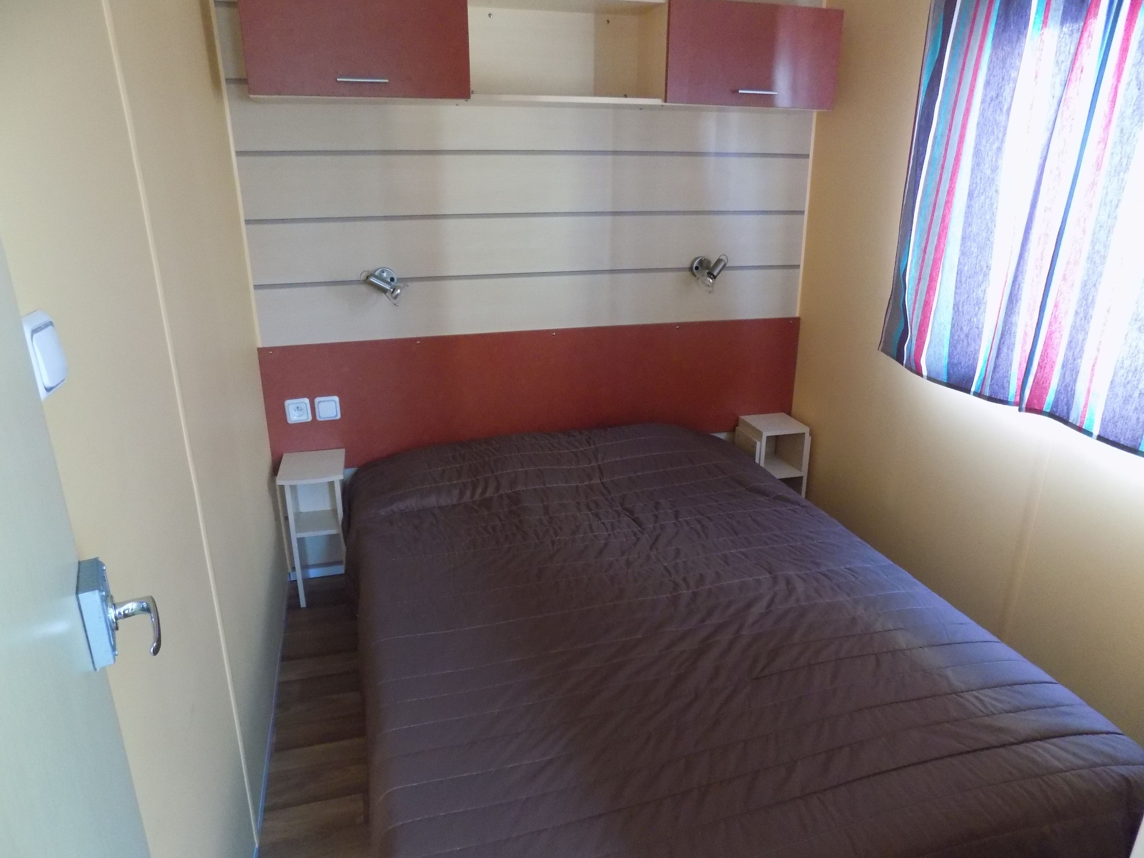 A bedroom with a bed, a nightstand, a small table, and a window with striped curtains.