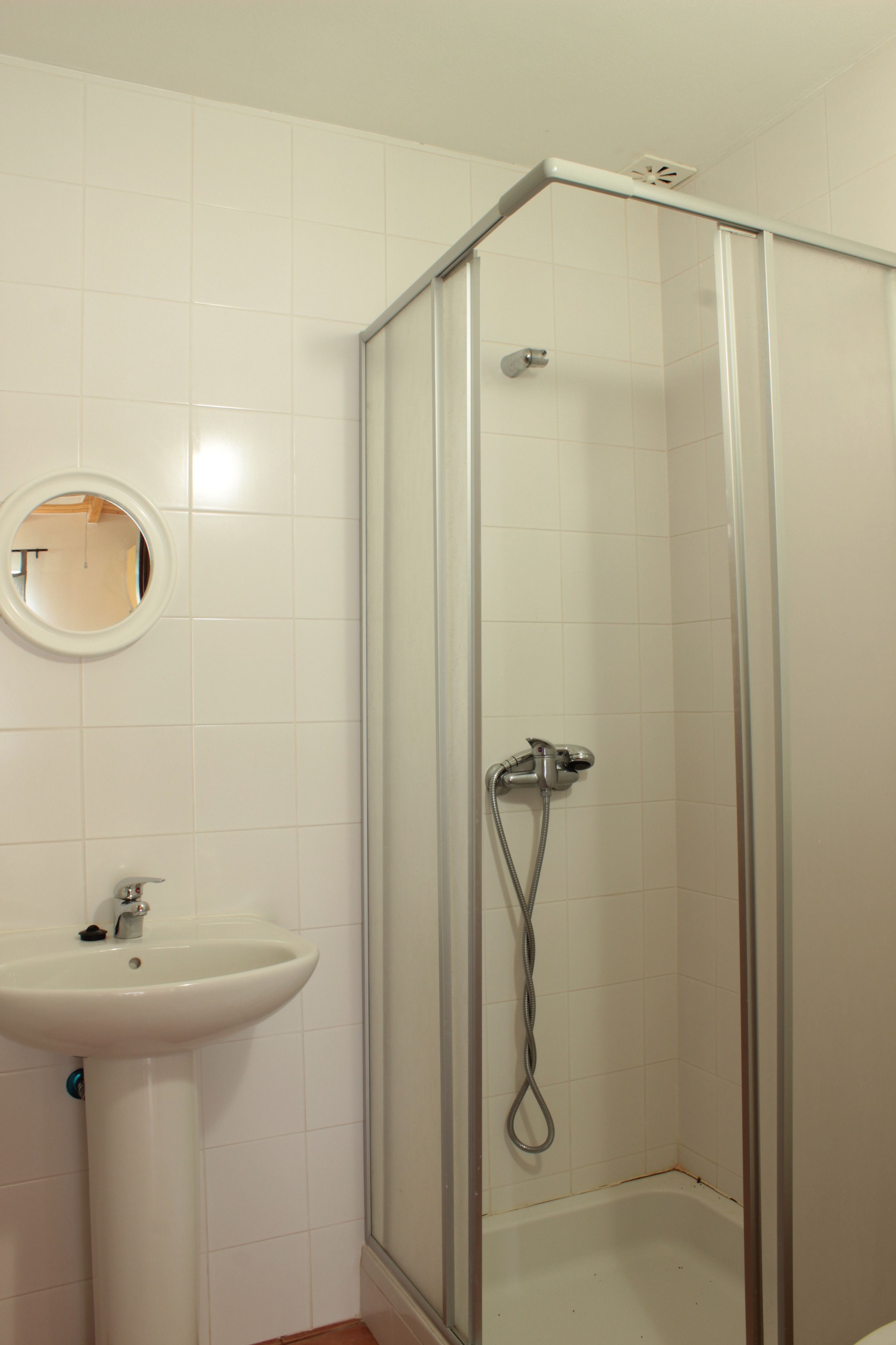 A bathroom with a glass-enclosed shower, a pedestal sink, and a round mirror.