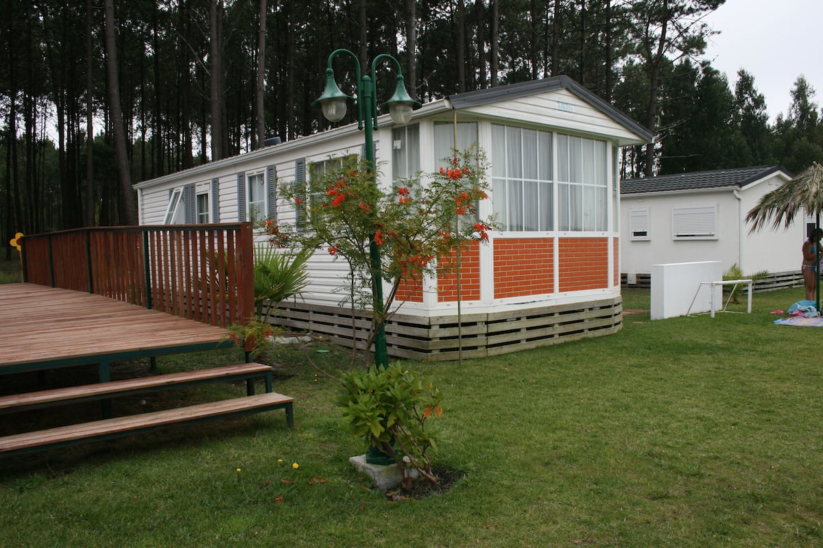 Ein Bungalow mit umzäunter Terrasse, einem kleinen Garten mit blühenden Pflanzen und einer Lampe.