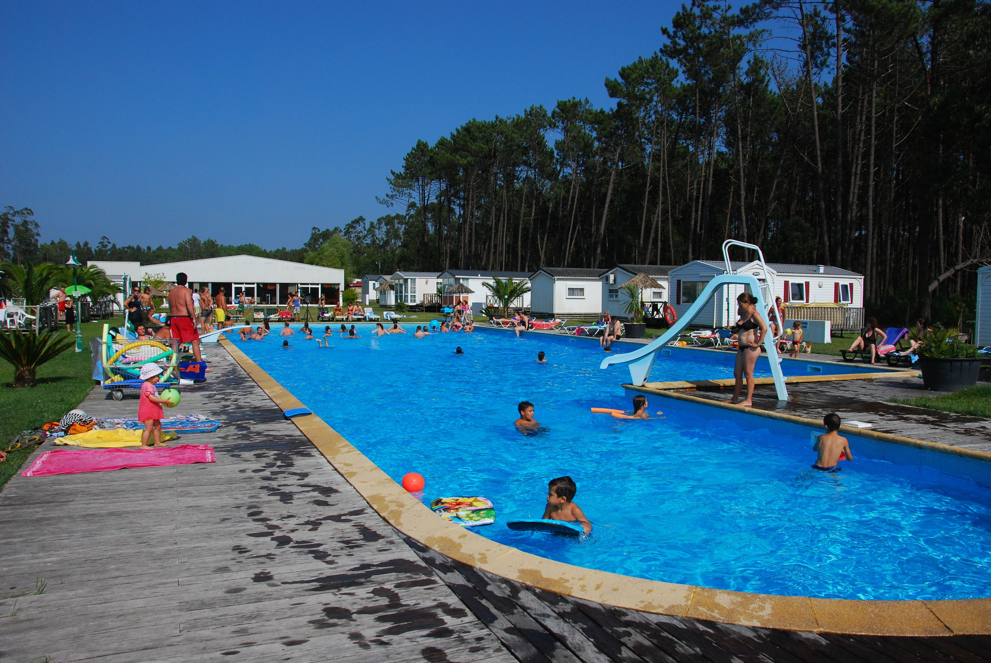 Un espace piscine comprenant plusieurs bassins, un toboggan aquatique et une terrasse en bois.