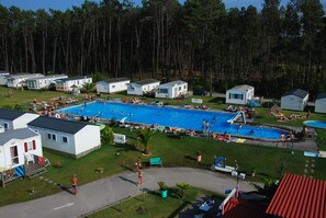 A large outdoor swimming pool surrounded by mobile homes, with people swimming and relaxing. - Land's Hause Bungalows (Alcobaça)