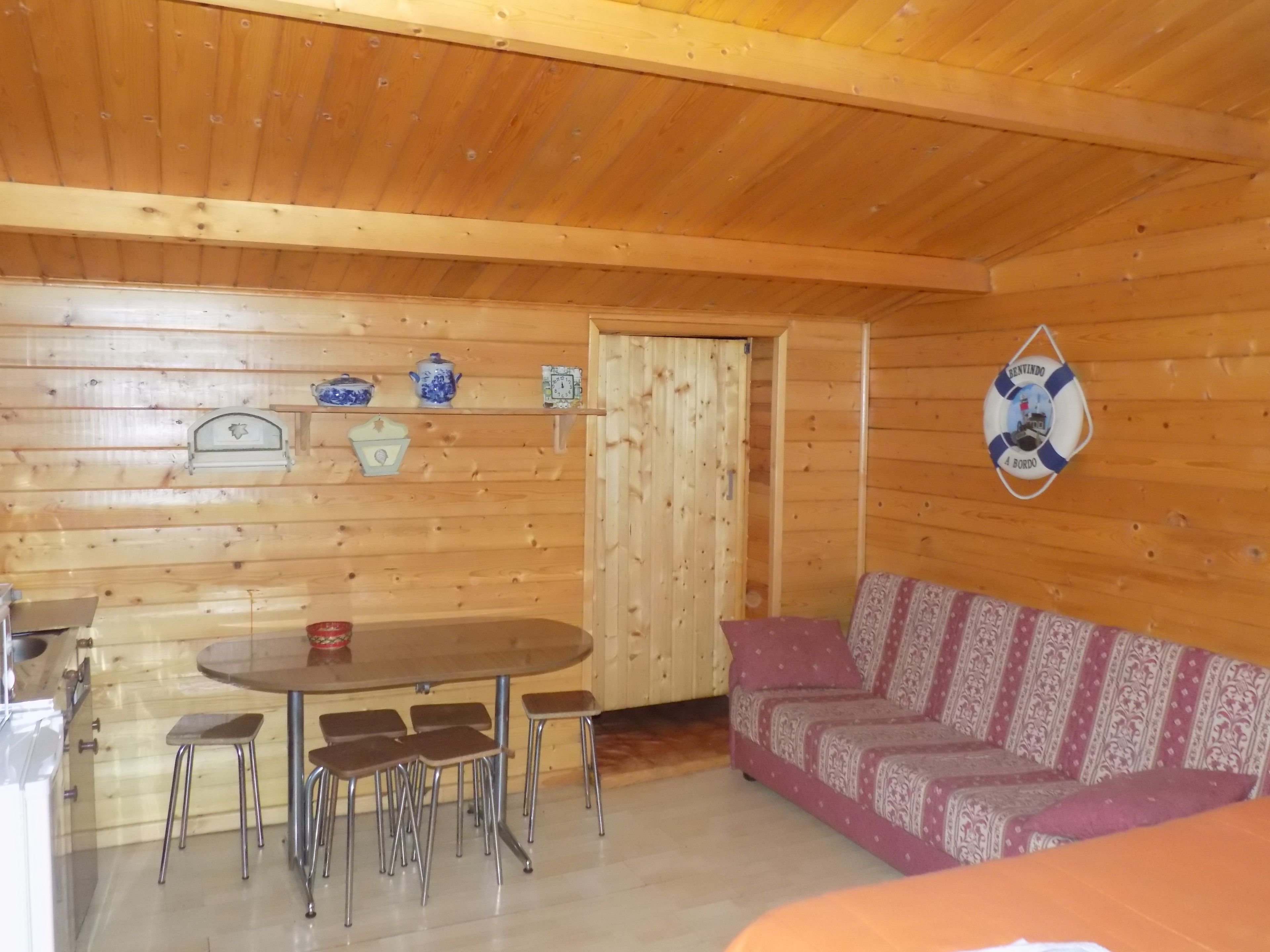 A wooden interior with a round dining table, four stools, a sofa, and a life preserver decoration on the wall.