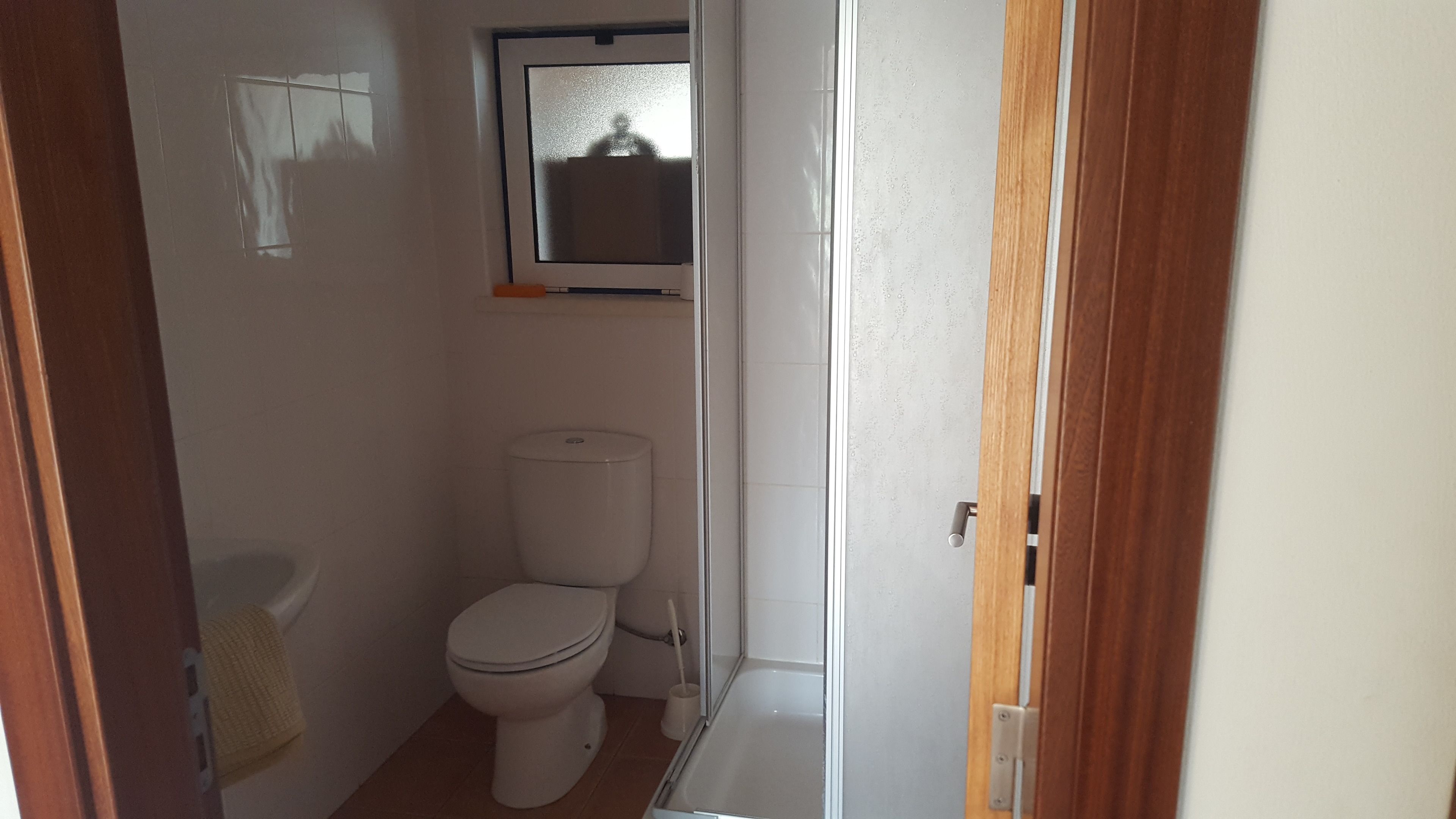 A small, clean bathroom with a toilet, a window, and a shower.