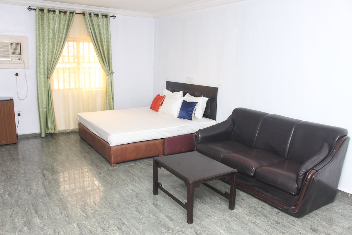 Un dormitorio con cama, sofá de cuero, mesa de centro de madera y ventana con cortinas.