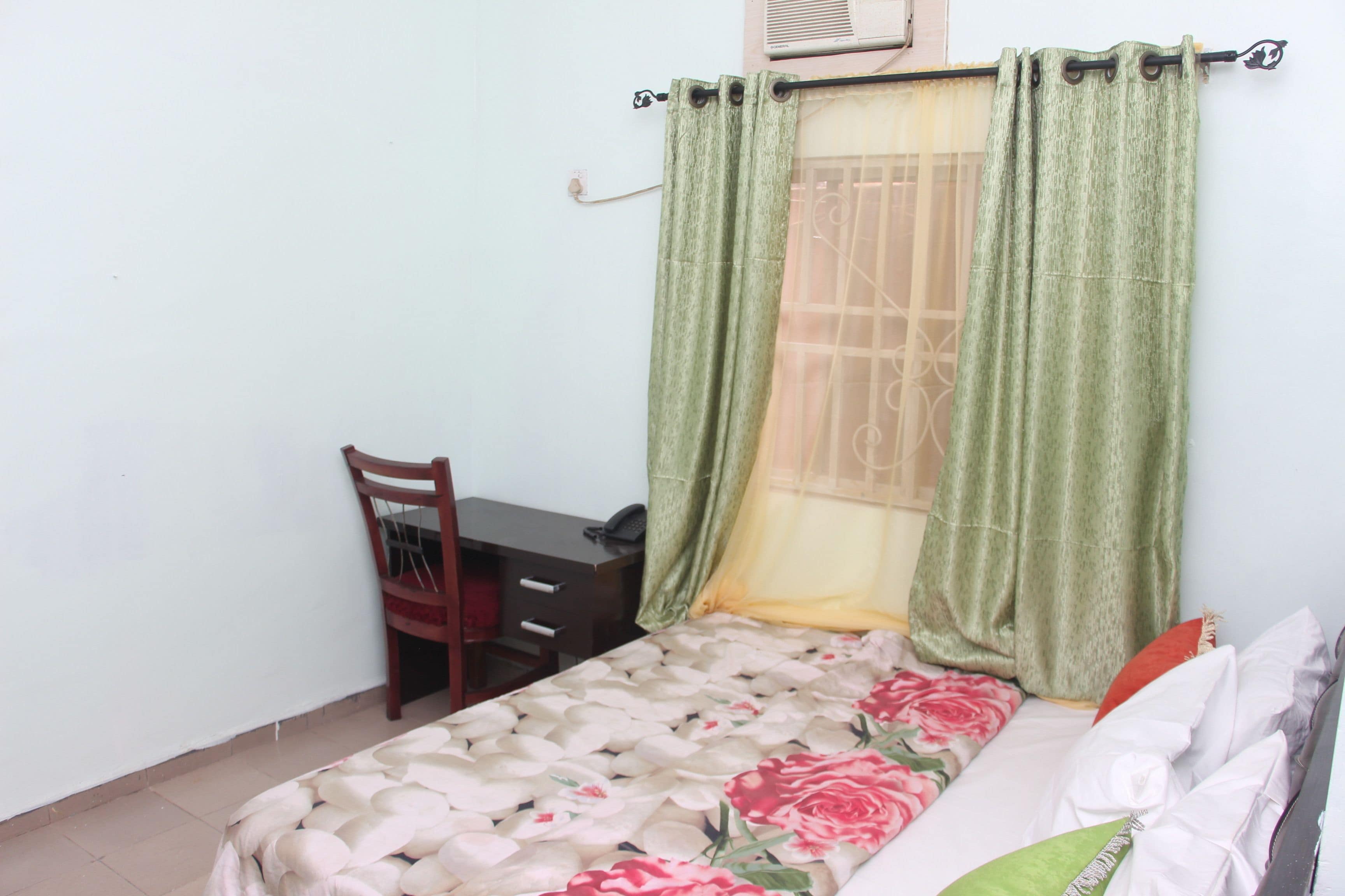 Une chambre à coucher avec un lit, une chaise, un bureau et une fenêtre avec des rideaux.