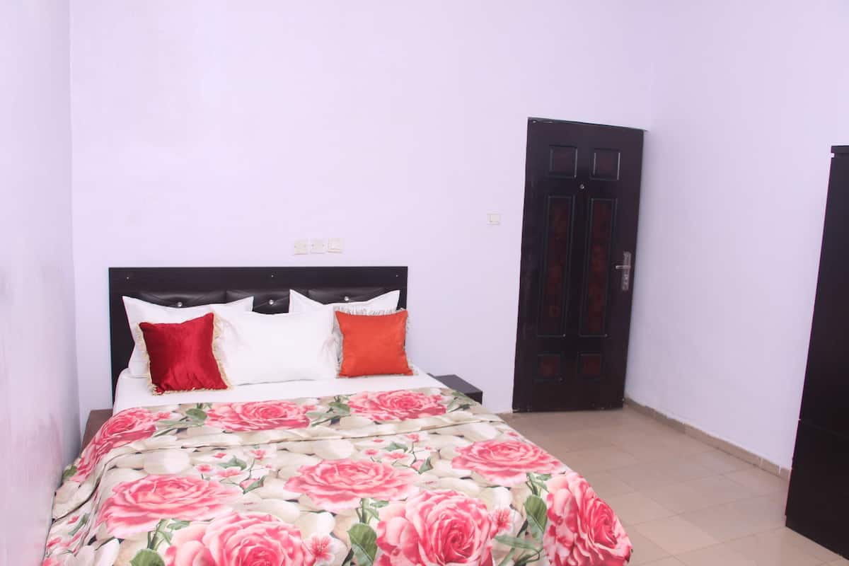 Un dormitorio con cama, mesita de noche, una puerta y un enchufe.