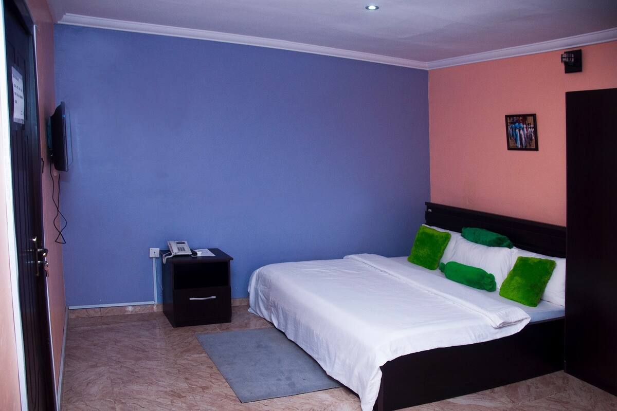 A bedroom with a bed, a nightstand, a telephone, and a wall-mounted TV.