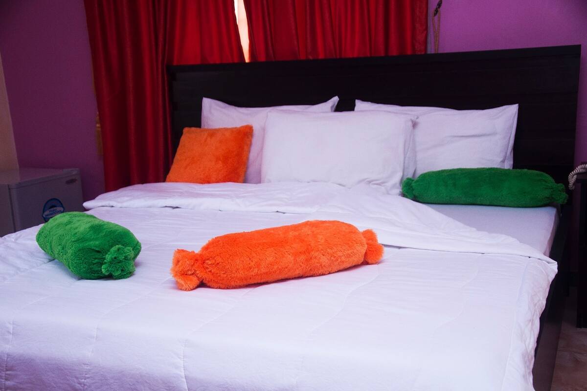 A bed with white bedding, a black headboard, and two pillows in green and orange.