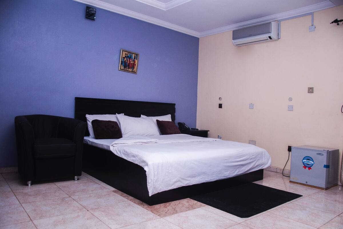 A bedroom with a bed, a chair, a small cabinet, and a painting on the wall.