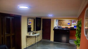 A hotel lobby with a reception desk, a small table with a chair, a door labeled 'RESTAURANT', and a wall with framed pictures. - Lamia Inn (Lagos)
