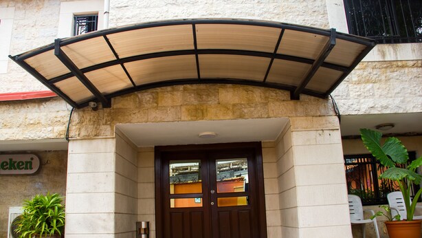 A hotel entrance with a wooden double door, a covered entrance area, and a potted plant to the right. - Lamia Inn (Lagos)