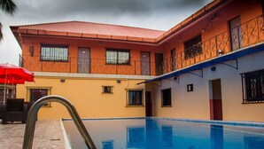 A swimming pool with a metal ladder, a red umbrella, and a building with a red roof and balconies. - Lamia Inn (Lagos)