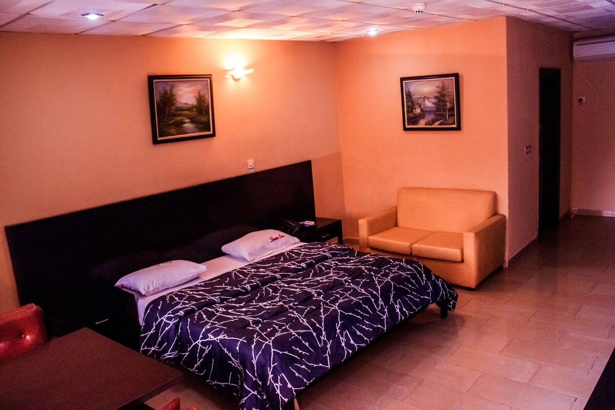 Une chambre d’hôtel avec un lit, une chaise et deux tableaux accrochés aux murs.