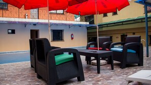 An outdoor seating area with wicker furniture and red umbrellas. - Lamia Inn (Lagos)