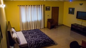 A hotel room with a bed, a chair, a TV, and a desk. - Lamia Inn (Lagos)