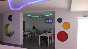 Un comedor moderno con mesas y sillas, un televisor en la pared y decoraciones circulares coloridas en las paredes.