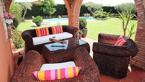 Un patio con mobiliario de mimbre, una mesa y vistas a una piscina y jardín.