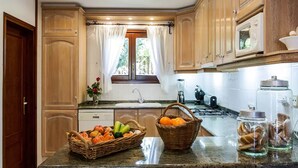 Una cocina con armarios de madera, encimera de granito, una ventana con cortinas y diversos electrodomésticos.
