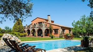 Una casa grande con piscina, arcos de piedra y un jardín bien cuidado.